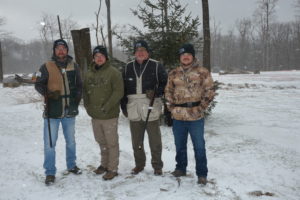 Photo of four clays shooters with snow and trees in background